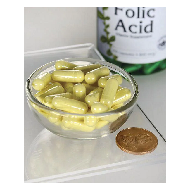 A small glass bowl of yellow capsules is next to a coin for size comparison, with a Swanson Folic Acid - 800 mcg 250 capsules bottle, essential for pregnancy health and rich in vitamin B9, in the background.