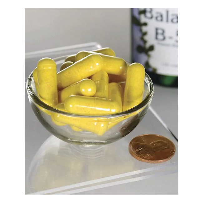 A small glass bowl containing Swanson Balance Vitamin B-50 Complex capsules is next to a coin for size reference, with the bottle partially visible in the background.