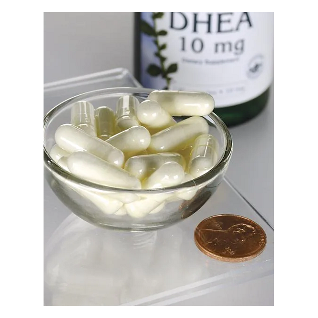 A small glass bowl with white capsules sits beside a penny for scale, while a Swanson "DHEA 10 mg 120 Capsules" bottle, known for promoting hormonal balance as the youth hormone supplement, is partially visible in the background.