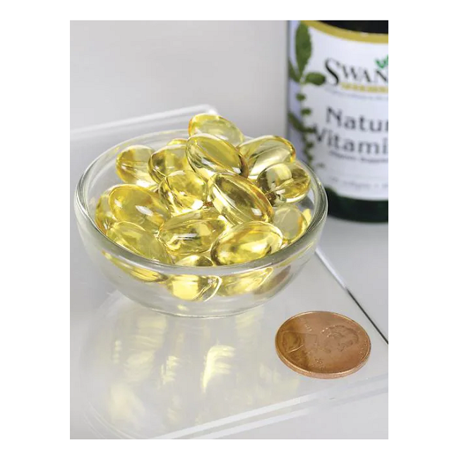 A small glass bowl holds yellow capsules beside a penny for scale, highlighting their compactness. A "Swanson Natural Vitamin E-400 IU 100 Softgels" bottle peeks in the background, suggesting the antioxidant-rich tocopherols these supplements offer.