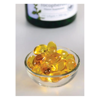 Thumbnail for A small glass bowl with Swanson's Vitamin E-400 Mixed Tocopherols softgels, rich in antioxidants, sits on a white surface. A blurred bottle is visible in the background.