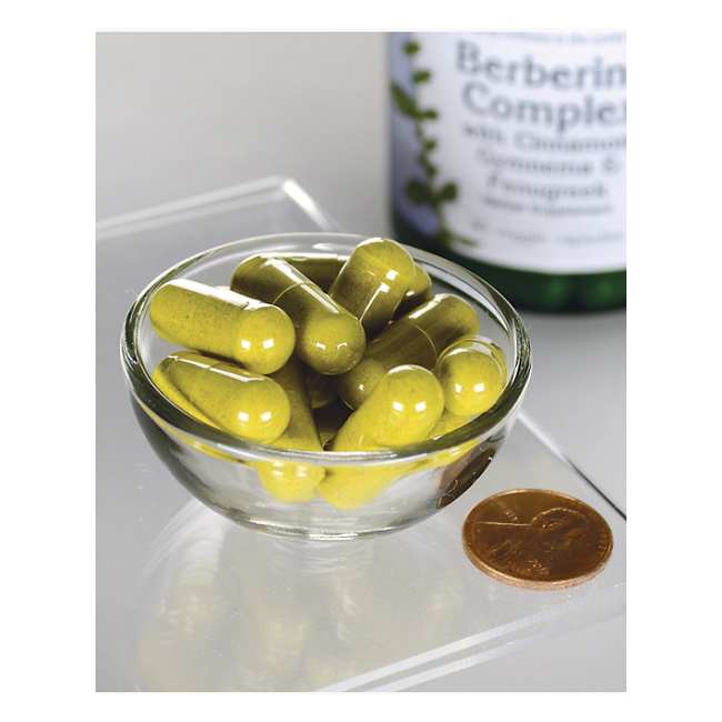 A small glass bowl with yellow capsules, promoting cardiovascular health, sits next to a penny for scale. In the background, a blurred bottle is labeled "Swanson Berberine Complex with Cinnamon, Gymnema & Fenugreek 90 Veggie Capsules," an Ayurvedic supplement.