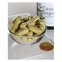 Thumbnail for A small glass bowl of green capsules sits next to a penny for scale, offering gentle digestive support. A blurred bottle in the background is labeled 