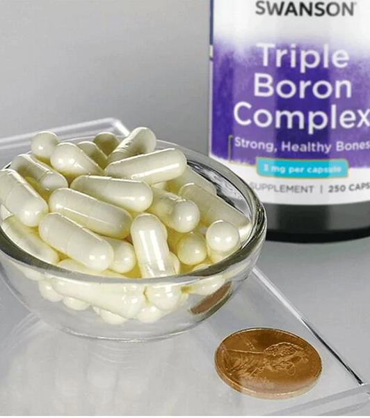 A bowl of white capsules is next to a coin and a bottle labeled "Swanson Boron Triple Complex 3 mg 250 Capsules," a dietary supplement for improved bone health.