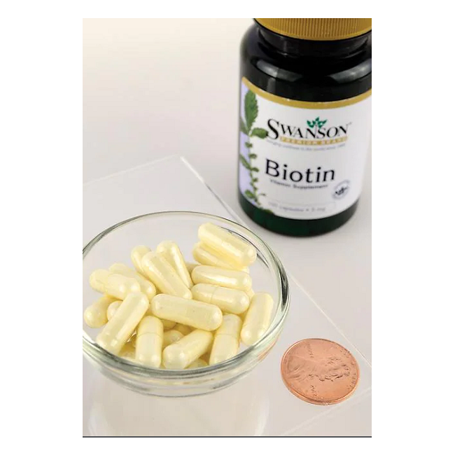 A bottle of Swanson Biotin 5000 mcg 100 Capsules sits beside a bowl, with a penny for scale. This Vitamin B7 powerhouse supports healthy hair, skin, and nails, making it essential for your daily regimen.