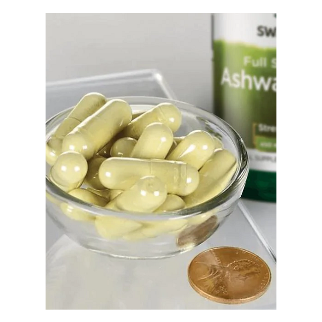 A small glass bowl of yellow capsules is next to a Swanson Ashwagandha 450 mg bottle containing 100 capsules, an adaptogen from Ayurvedic medicine, with a penny for size reference.