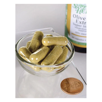 Thumbnail for A small glass bowl contains several olive green capsules beside a penny for scale. In the background, a partially visible bottle labeled 