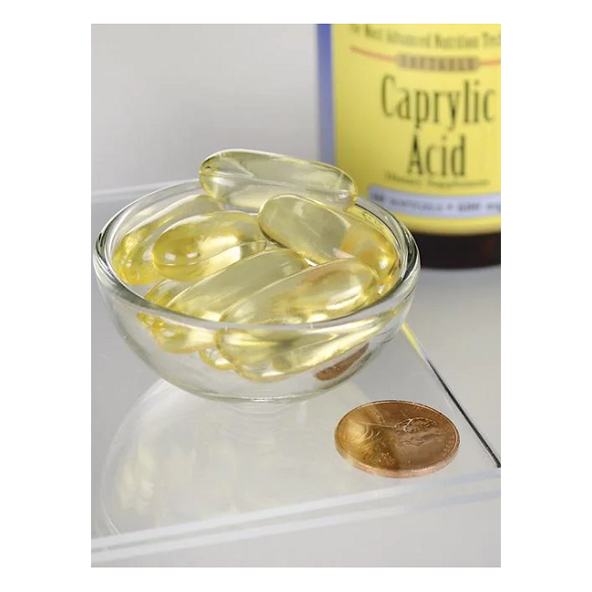 A small glass bowl holds several yellow capsules, with a penny nearby for size comparison. In the background, a partially visible "Swanson Caprylic Acid 600 mg 60 Softgels" bottle, praised for its antifungal properties, can be seen.