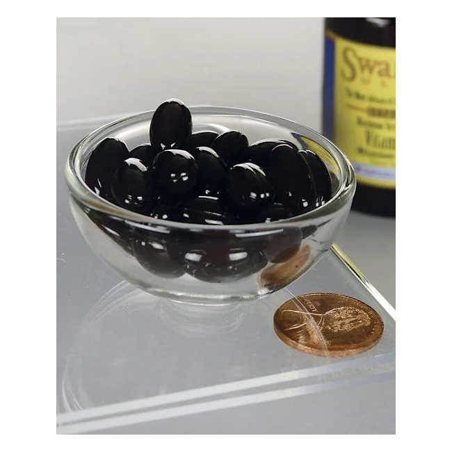 A glass bowl of Swanson's Real Food Vitamin K2 200 mcg pills sits beside a copper penny on a reflective surface, with the bottle partially visible in the background.