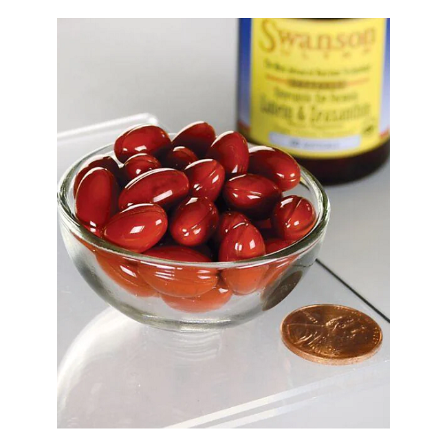 A glass bowl with red capsules, Swanson's Synergistic Eye Health - Lutein & Zeaxanthin 60 Softgels, sits beside a penny with a blurry supplement bottle in the background.