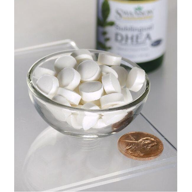 Un bol de pilules blanches à côté d'un flacon de Swanson DHEA - 25 mg 60 pastilles arôme cerise.