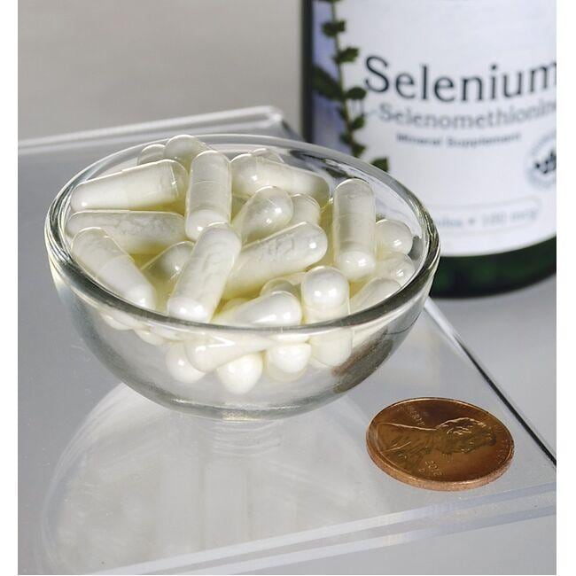 Swanson Sélénium - 100 mcg 200 gélules L-Sélénométhionine dans un bol à côté d'un penny, offrant un soutien antioxydant pour la santé cardiovasculaire.