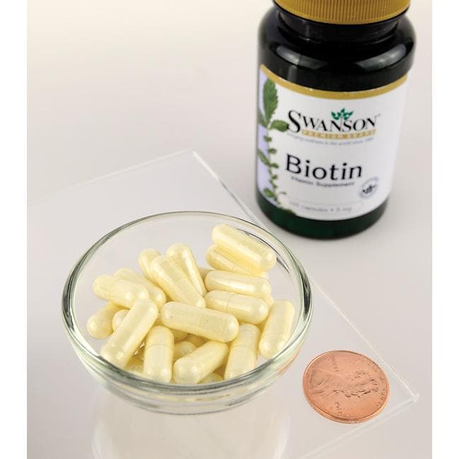 Un flacon de complément alimentaire Swanson Biotine - 5 mg 100 gélules à côté d'un penny sur une table.