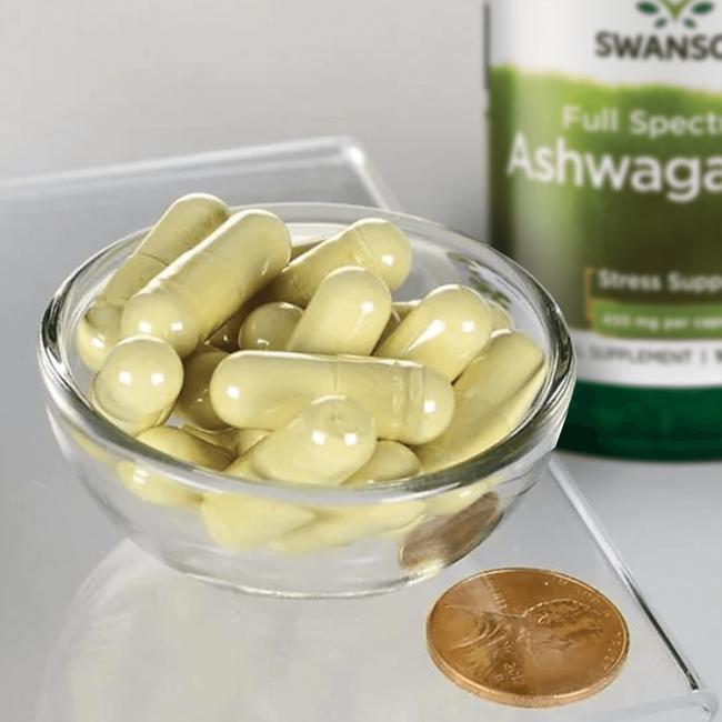 Un bol de Swanson Ashwagandha - 450 mg 100 gélules avec une pièce de monnaie à côté.