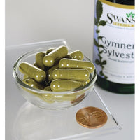 Vignette d'un flacon de Swanson Gymnema Sylvestre Leaf - 400 mg 100 gélules avec un penny dans un bol.