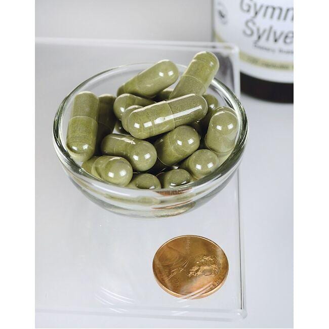 Un bol de Swanson Gymnema Sylvestre Extract - 300 mg 120 gélules à côté d'une pièce de monnaie.