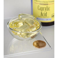 Vignette de Swanson's Caprylic Acid - 600 mg 60 softgel dietary supplement capsules dans un bol à côté d'une pièce de monnaie.