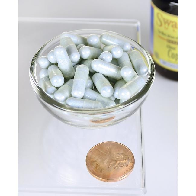 Un bol de Swanson Copper - 2 mg 60 capsules Albion Chelated à côté d'un penny.
